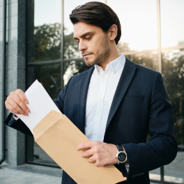 young-handsome-bearded-brunette-man-white-shirt-classic-jacket-standing-dreamily-opening-envelope-with-glass-building-background-1