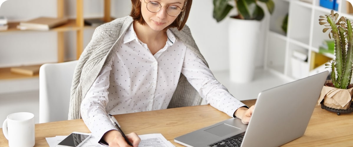 Frau arbeitet am Laptop und macht Notizen am Schreibtisch