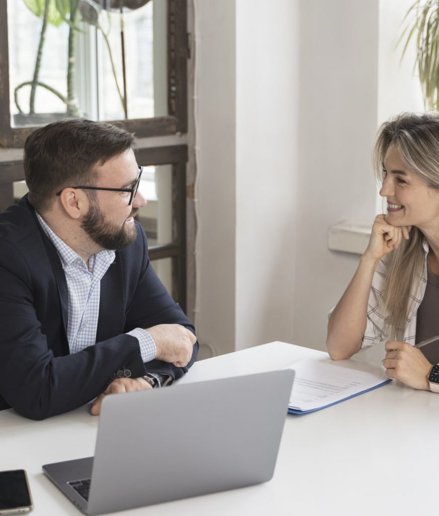 person-presenting-their-job-resignation Gespräch im Büro: Mann und Frau sitzen am Tisch mit Laptop und Dokumenten.