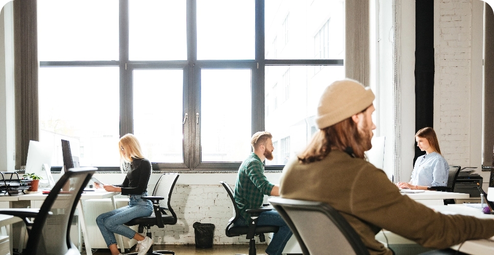 colleagues-work-office-using-computers-looking-aside@2x Team arbeitet im offenen Büro am Fenster