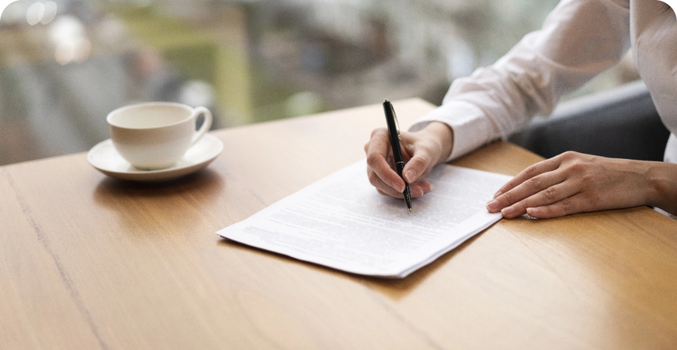 modern-unrecognisable-woman-taking-notes@2x Hand unterschreibt Dokument am Tisch