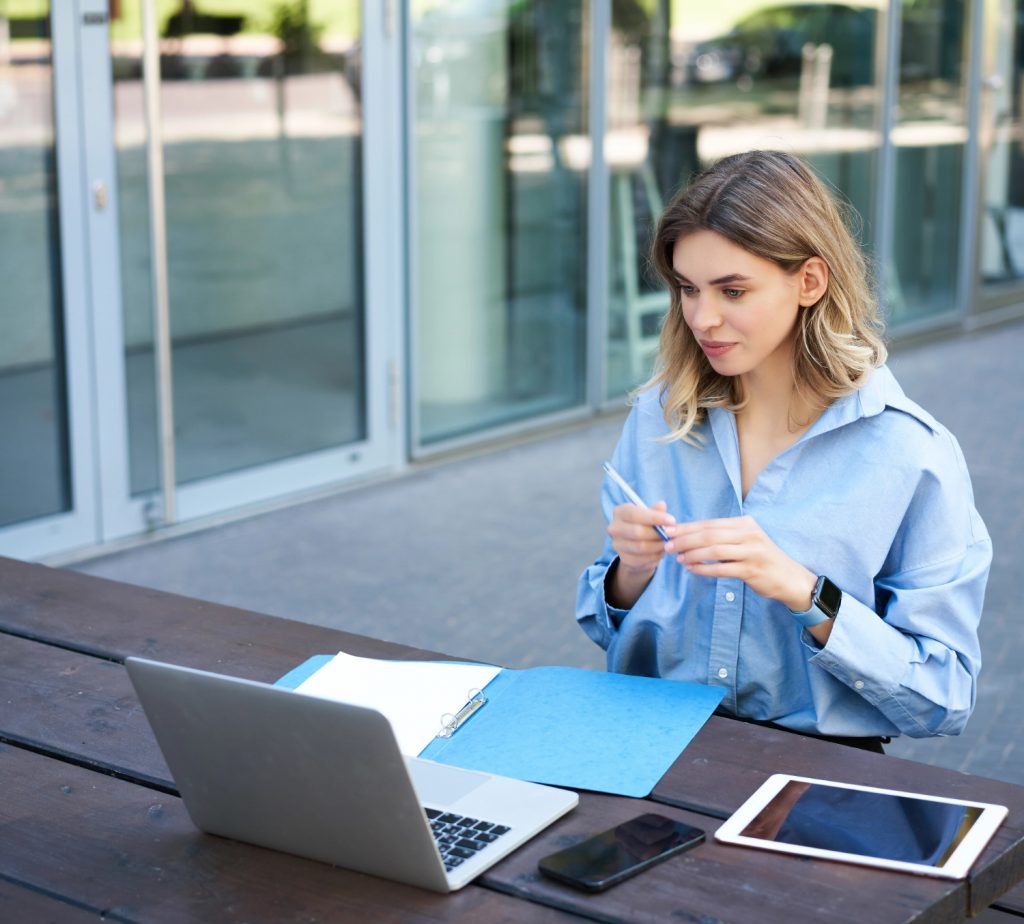 young-businesswoman-attend-online-video-conference-writing-down-working-taking-notes-her-document@2x Frau arbeitet am Laptop und macht Notizen am Schreibtisch